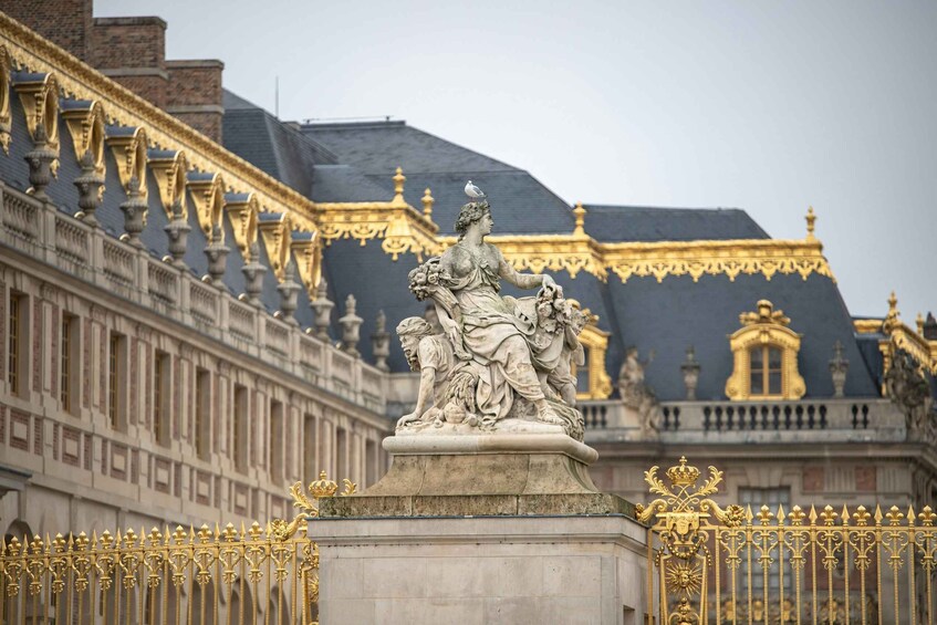 A classical statue with a bird on its head, set against a building with ornate golden details and a dark roof. 5