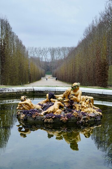 A canal with statues of figures surrounded by grapes, reflecting in the water. 3
