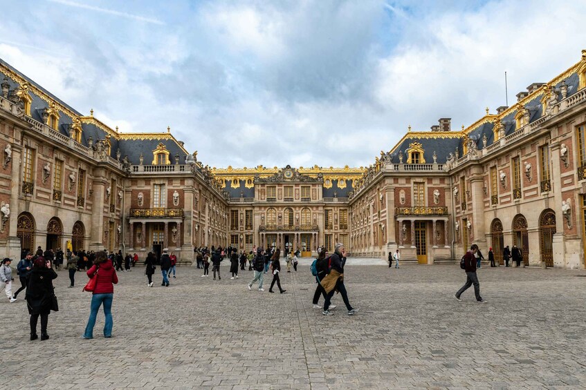 A historic courtyard with ornate architecture, a large open space, and people walking. 1