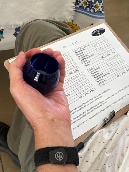 A person holding a blue glass, sitting with a clipboard containing a sensory evaluation form. 5