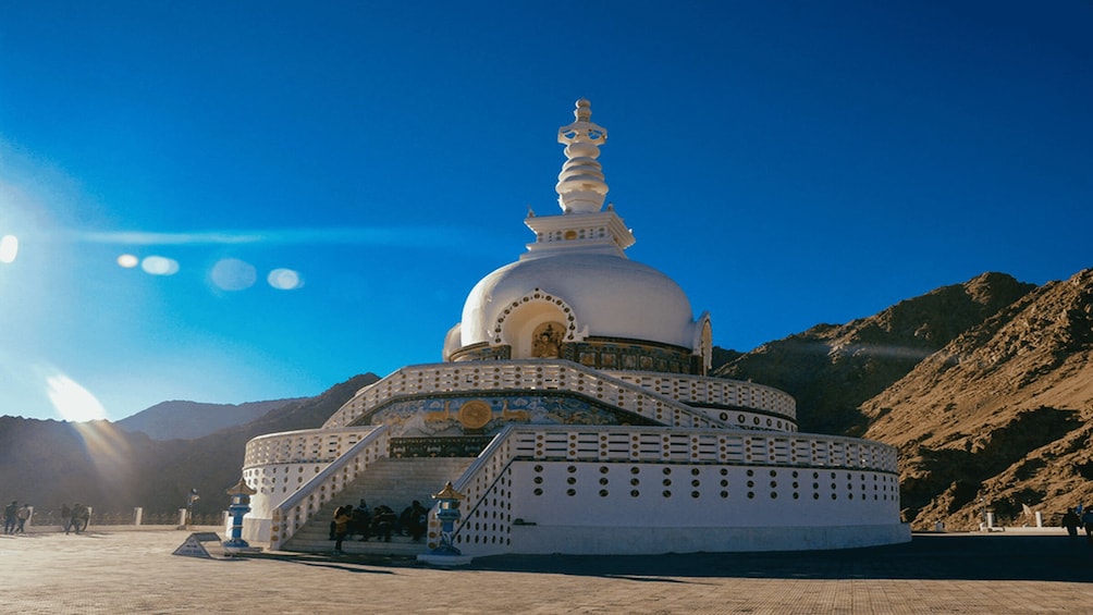 A white stupa with a golden spire, surrounded by mountains and a clear sky. 1
