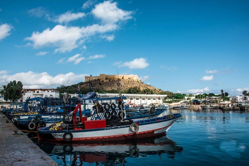 A harbor with boats, a fort on a hill, and buildings along the waterfront. 2