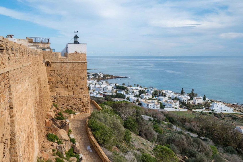 A coastal town with a historic stone wall and a lighthouse. 1