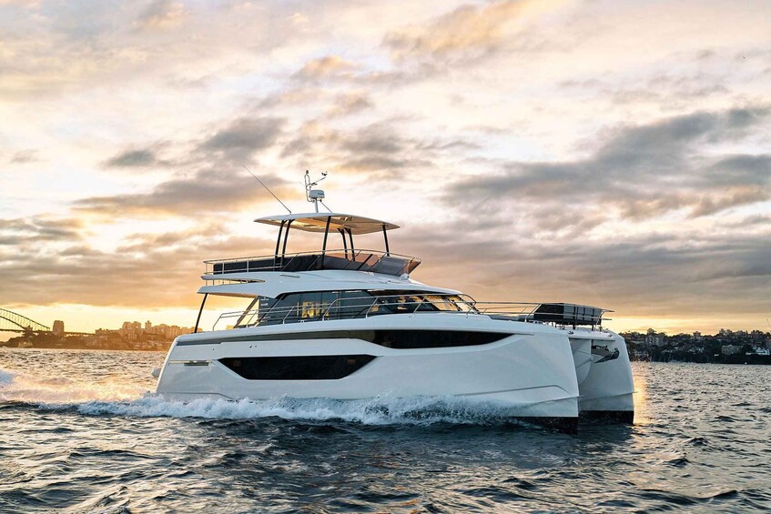 A large white yacht moving through a body of water with a city skyline and a bridge in the background during sunset. 2