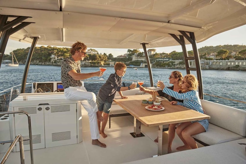 A group of people on a boat with a table, drinks, and a scenic waterfront view. 4