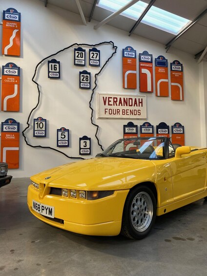 A yellow convertible car in a garage with a wall displaying numbered signs resembling a map. 3
