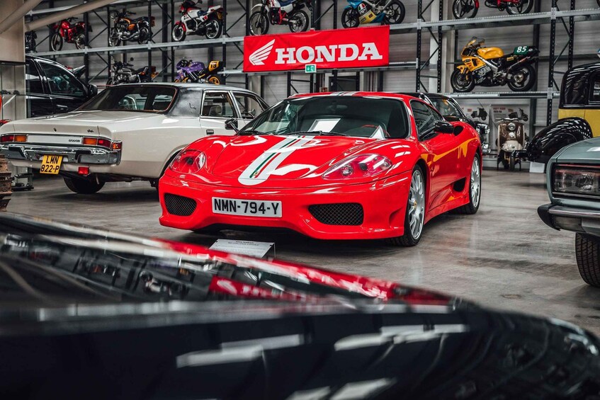 A red sports car with a license plate in a garage with various motorcycles and a Honda sign. 2