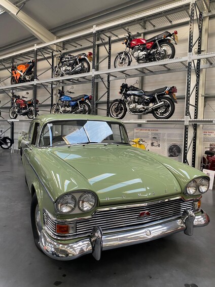 A vintage green car in a garage with motorcycles on shelves. 4