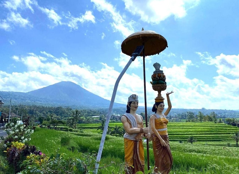 Two statues in traditional attire, a mountain, and terraced fields. 2