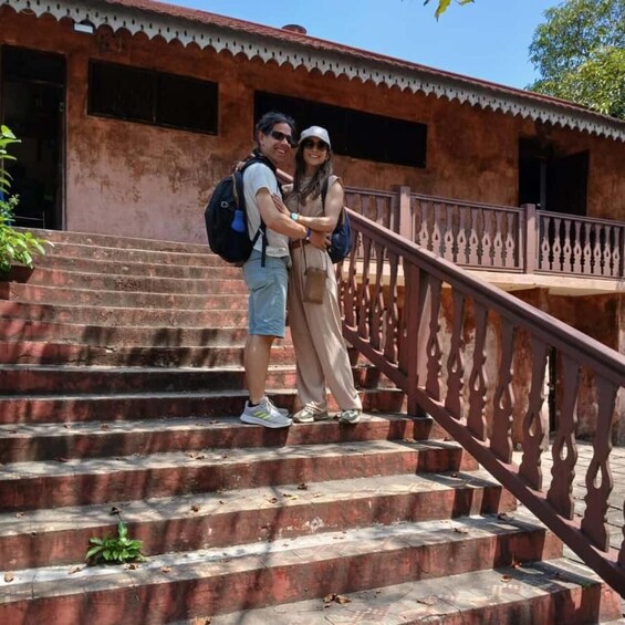 A couple embracing on a set of stairs with a decorative railing, leading to a building with a red-tiled roof. 4