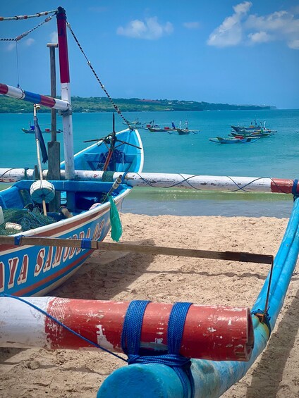 A beach with a blue and white boat named 'YAYA SAMUDRA' anchored near the shore, with other boats in the background and a clear sky. 3