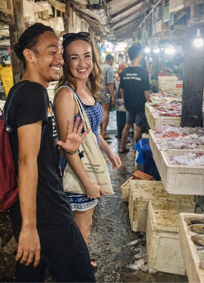 A couple standing in a market with seafood displayed on tables. 1
