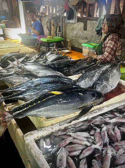 A market stall with fresh fish, including tuna and squid, displayed in a wooden crate. 2