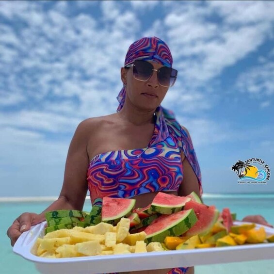En person som håller ett bricka med vattenmelon och ananas på en strand. 3