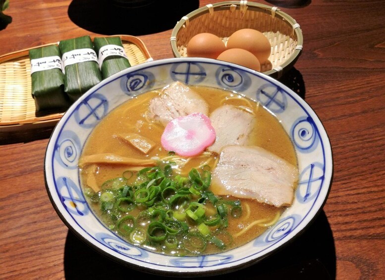 A bowl of ramen with sliced pork, green onions, and a radish on top, accompanied by tamagoyaki and tamagoyaki in a basket. 1