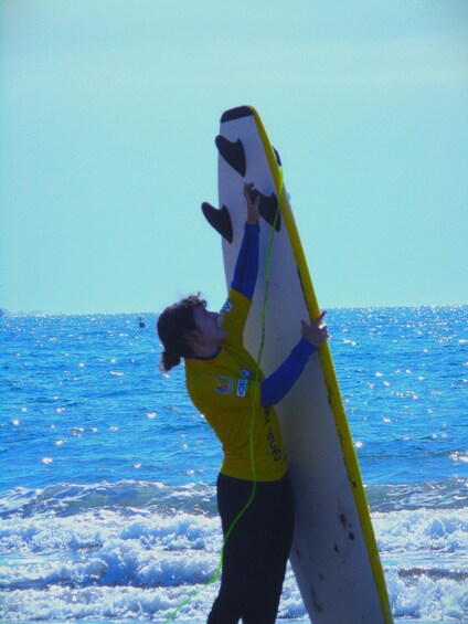 A person in a yellow wetsuit holding a surfboard. 3