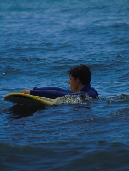 A person lying on a surfboard in the ocean. 5