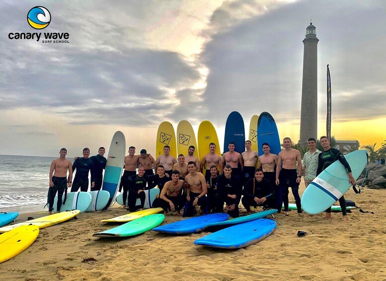 A group of people with surfboards on a beach with a lighthouse in the background. 1