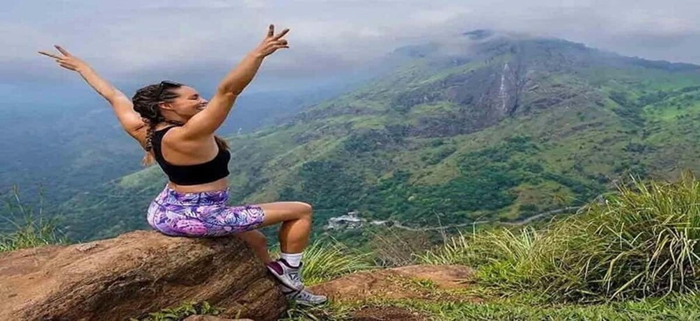 A person sitting on a rock with arms raised, overlooking a mountainous landscape. 5