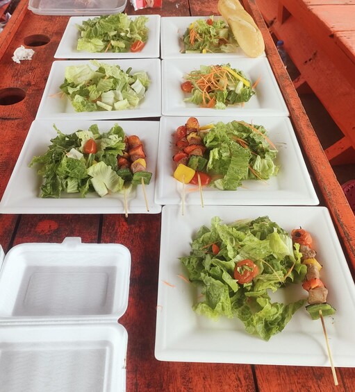 A wooden table with various plates of food, including salads and skewers. 1