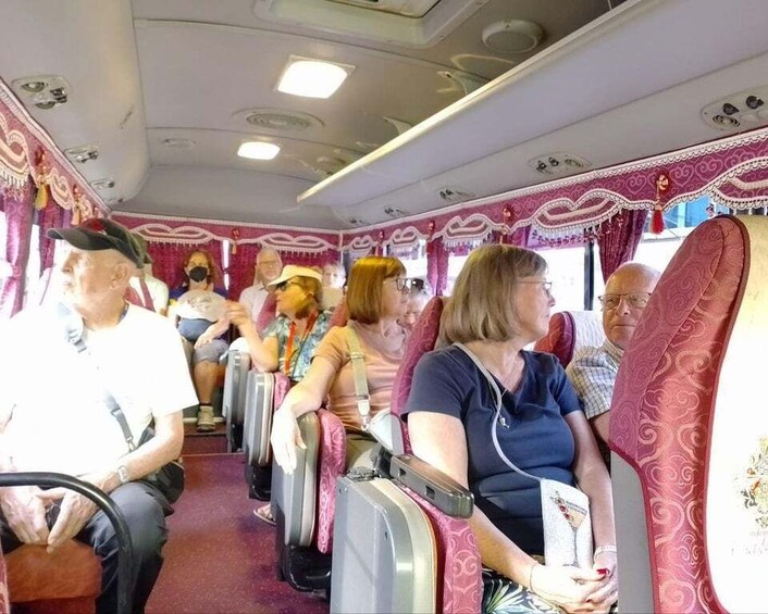 Passengers seated on a train with red and gold patterned upholstery. 2