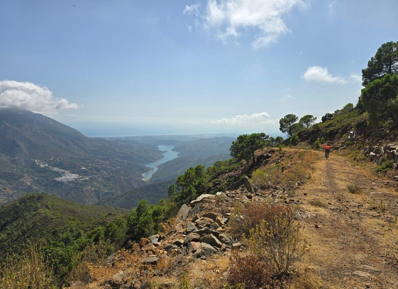A hiker on a rocky trail with a valley and river in the distance. 1