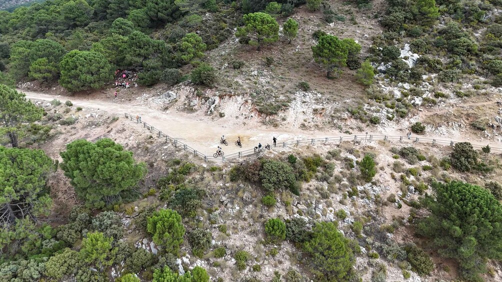 A mountainous landscape with a dirt path, sparse vegetation, and a fenced area with people and bicycles. 3