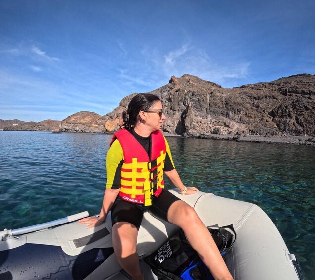 A person on a boat wearing a life jacket, with clear water and rocky hills in the background. 3