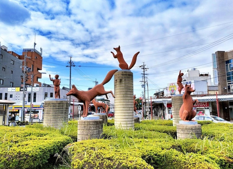 A street with statues of foxes on top of cylindrical stone bases, surrounded by greenery. 2