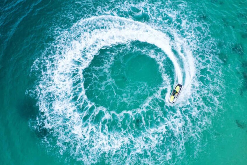 A circular wake pattern in turquoise water with a small boat creating the wake. 3