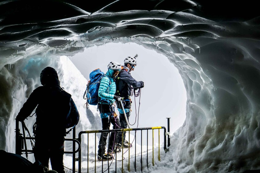 A group of people in ice cave with ice formations and a metal railing. 3