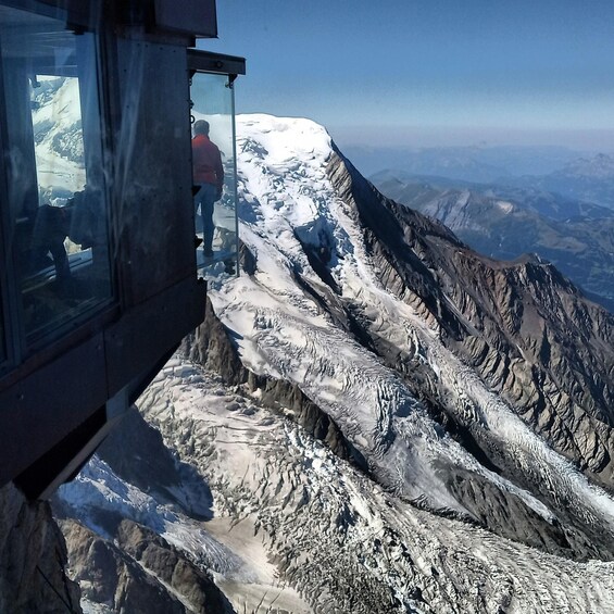 A person standing on a glass platform overlooking a snow-covered mountain range. 5