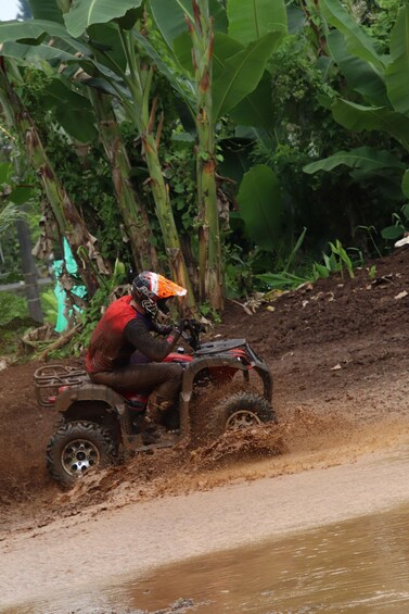 A person on a four-wheeled vehicle navigating a muddy terrain. 2