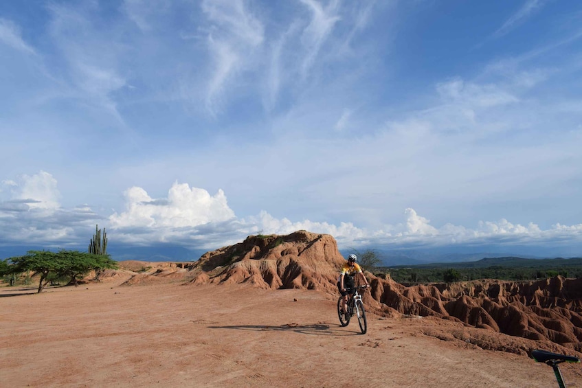 A cyclist on a dirt path with a mountainous backdrop and sparse vegetation. 1