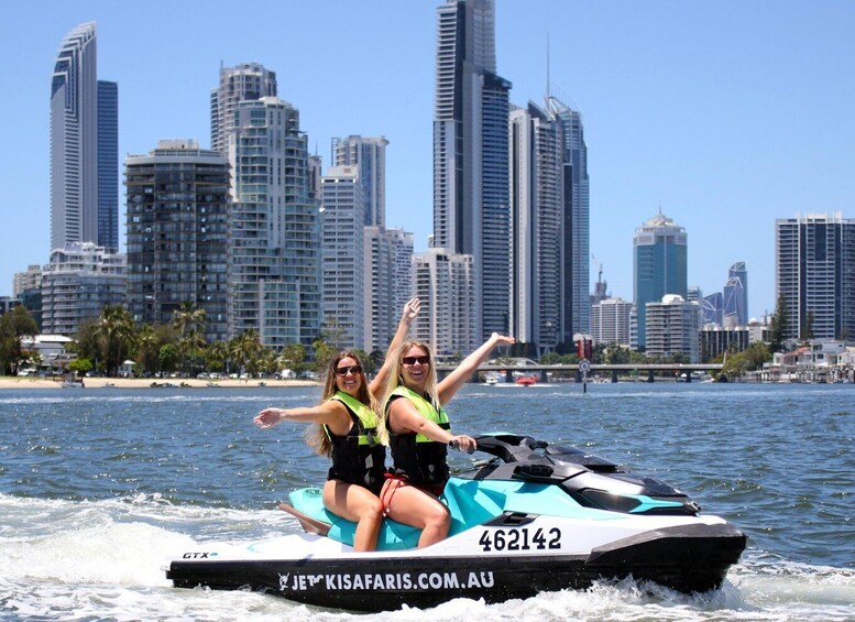 Two people jet skiing on a body of water with a city skyline in the background. 2