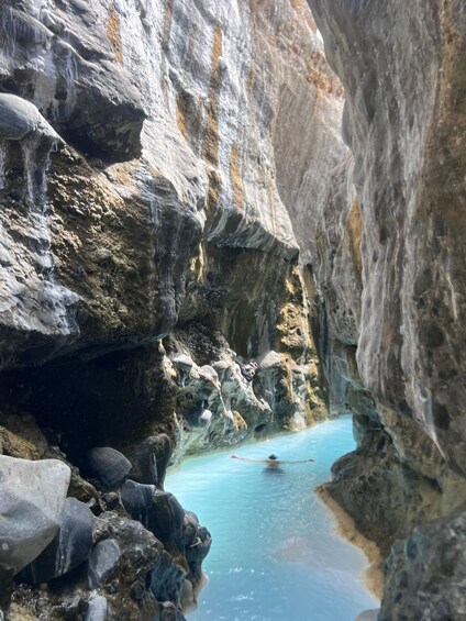 A narrow canyon with a clear blue pool and a person paddling in the water. 3