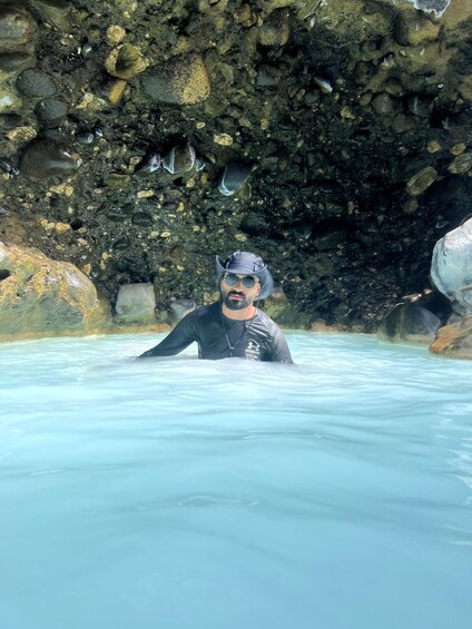 A person in a wetsuit standing in clear water with a rocky background. 5