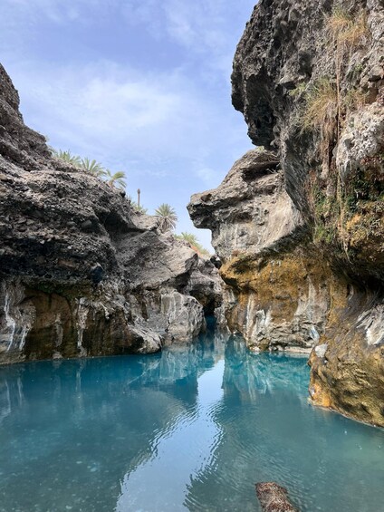 A rocky canyon with clear blue water and palm trees. 2