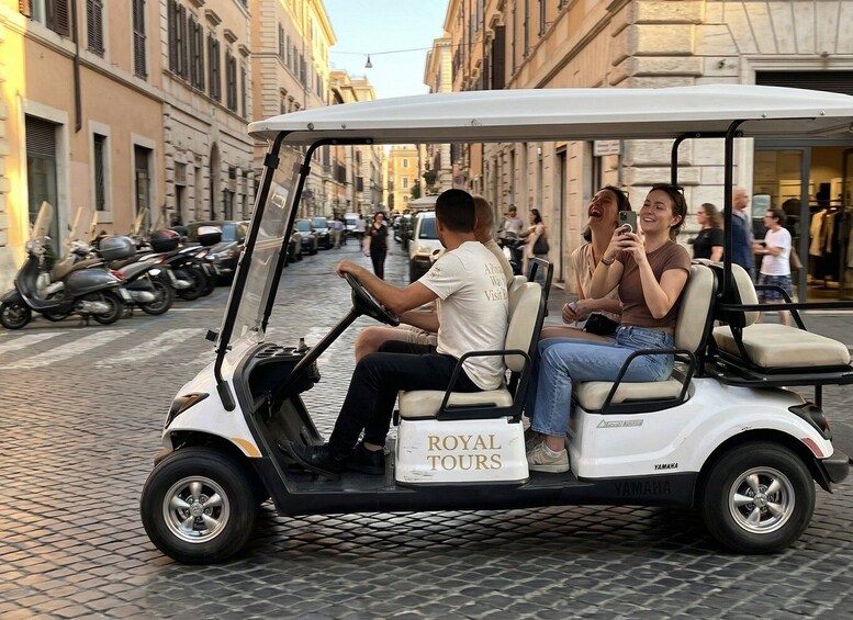 A golf cart with 'ROYAL TOURS' written on the side, parked on a cobblestone street with buildings and parked scooters in the background. 3