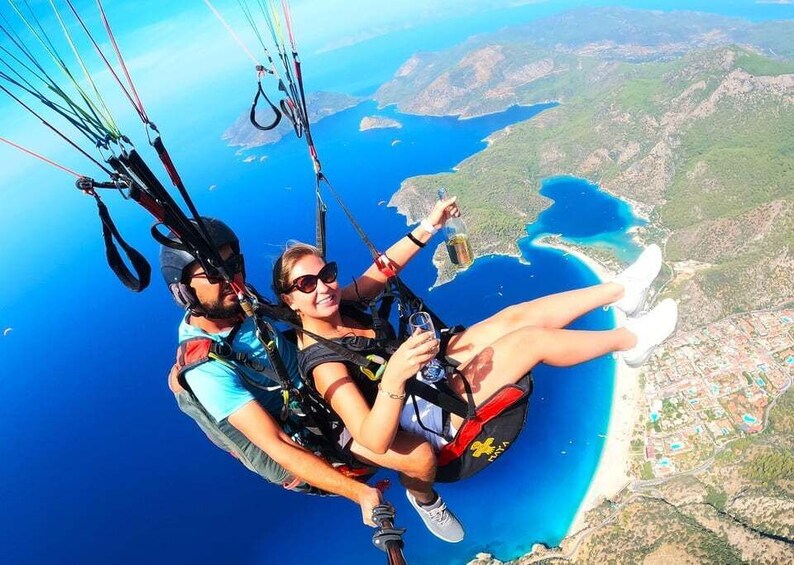 Two people paragliding over a coastal landscape with clear blue waters and a view of a town below. 3