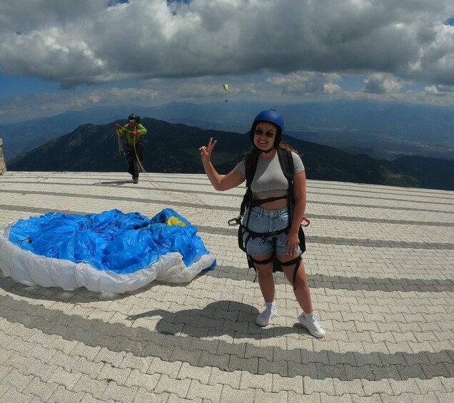 A person standing on a paved area with a parachute and a backpack, with mountains in the background. 4