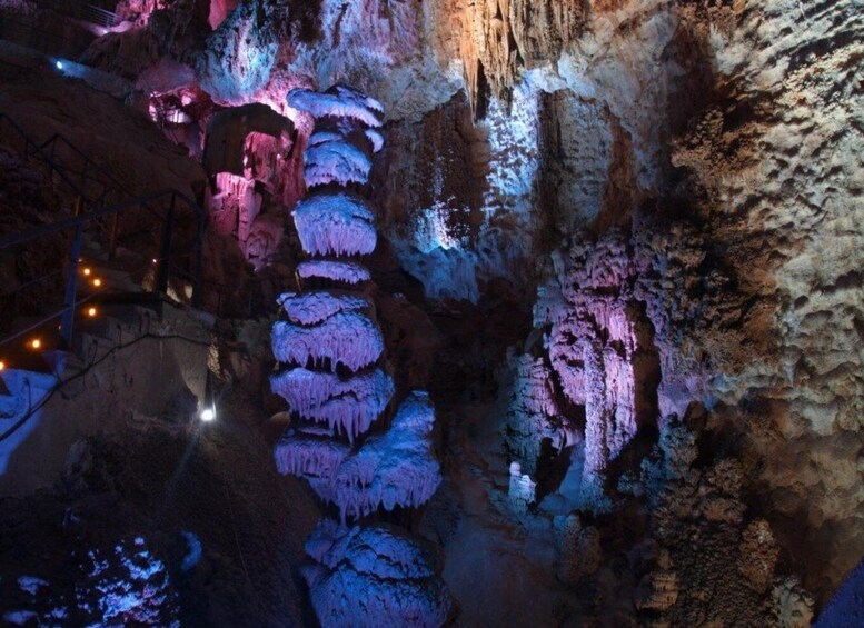 A cave illuminated with blue and pink lights, showcasing stalactites and stalagmites. 3