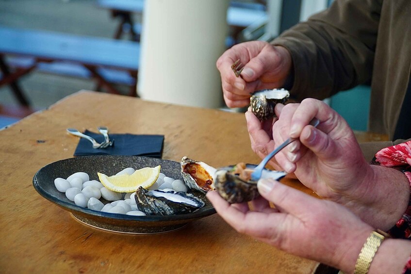 A person holding a shellfish with a fork, a bowl of ice, and a lemon slice on a wooden table. 4
