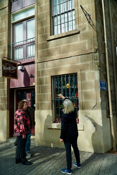 A woman looking through a barred window of a building with a sign for 'Woody Jane' and a blue sign indicating toilets. 2