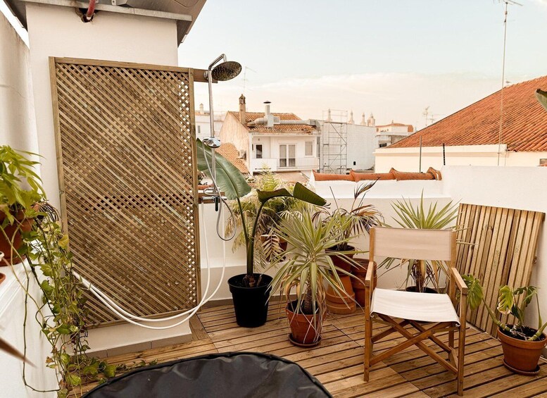 A rooftop terrace with a wooden deck, potted plants, a folding chair, and a retractable awning. 4