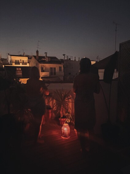 A person standing on a rooftop with a lantern in the foreground, overlooking a residential area at dusk. 5