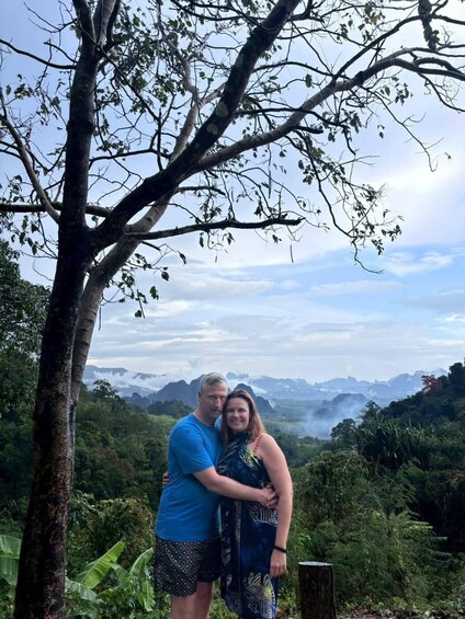 A couple embracing in a mountainous landscape with dense greenery and distant peaks. 2