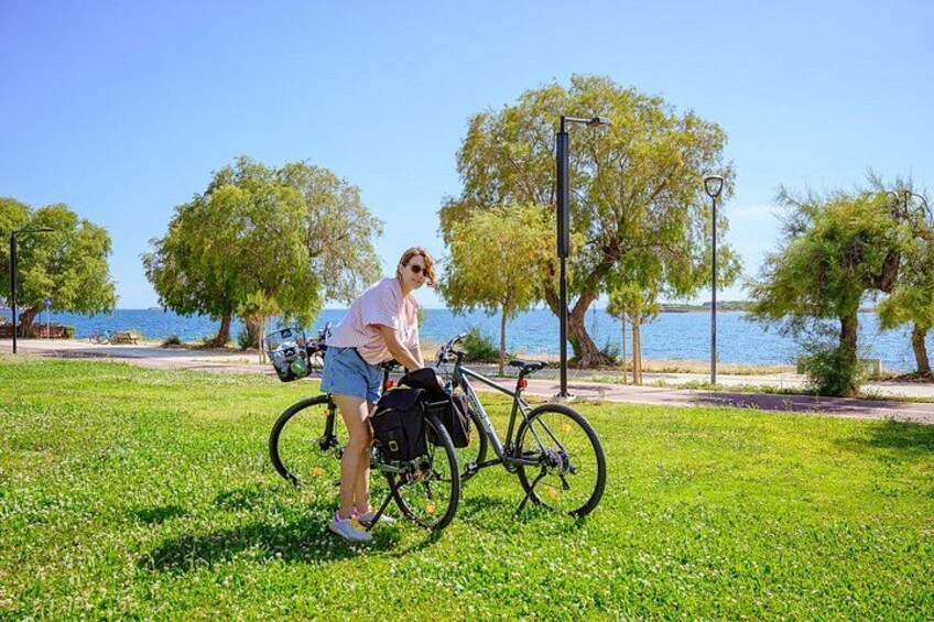 A person standing next to a bicycle in a grassy park with trees and a body of water in the background. 3