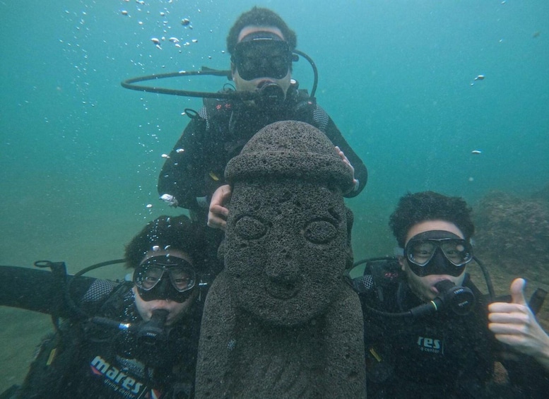 Divers underwater with a rock formation shaped like a face. 1