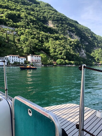 A boat docked near a waterfront with buildings and a forested hillside in the background. 2